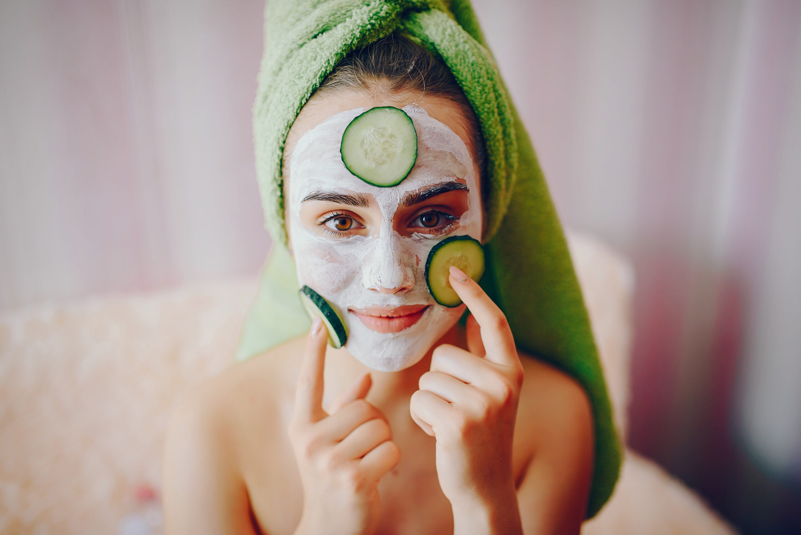 Beautiful girl sitting on the couch in the room. Lady in a green towel and with cucumber on her face